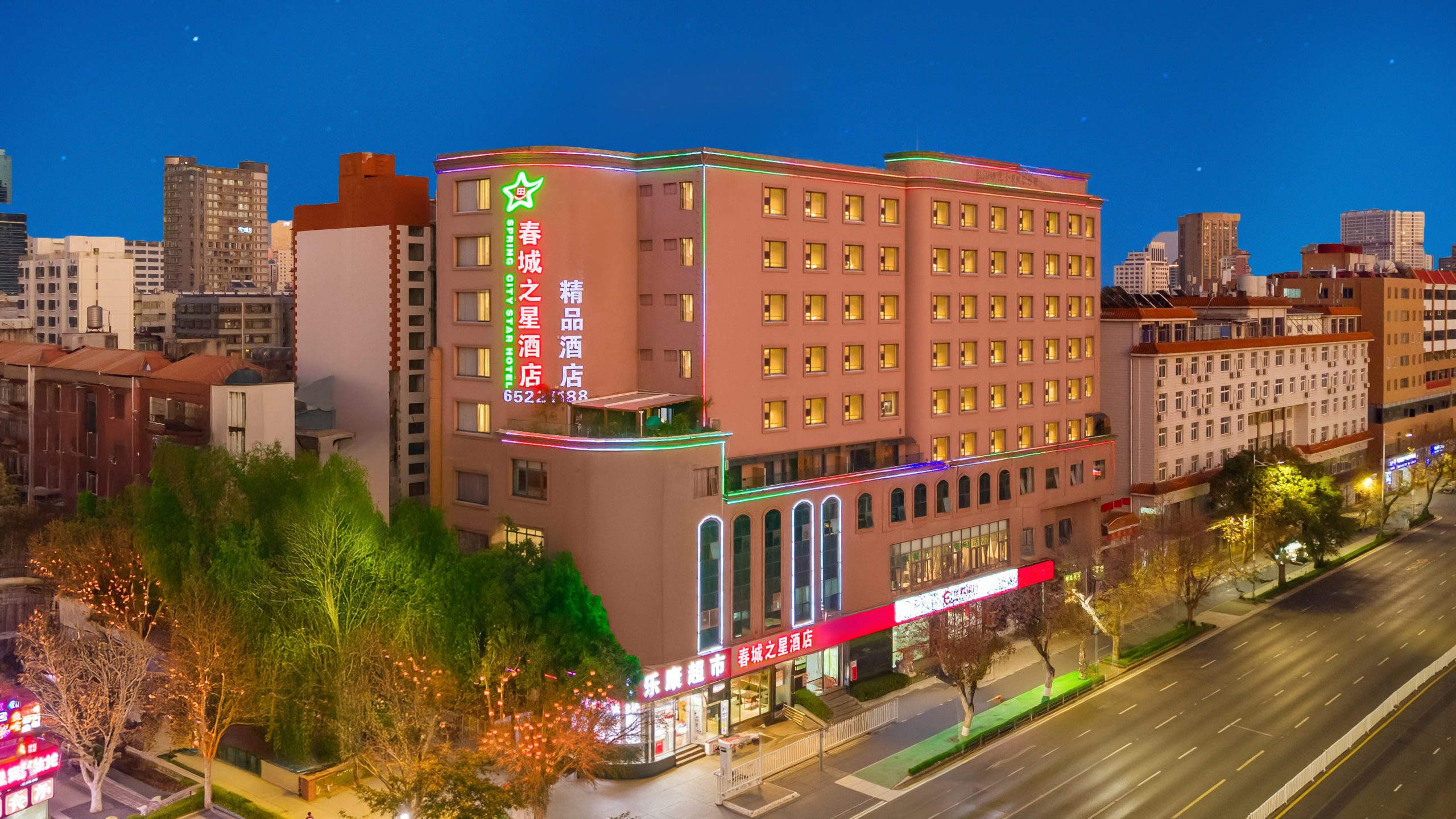 春城之星精品酒店黄昏航拍，建筑外观与周边绿树、街道夜景融为一体。